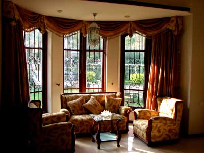 Very elegant treatment to this bay window, using swags with decorative trim to form a curved valance to hide the curved curtain track, and rich full heavy drapes to each side. 